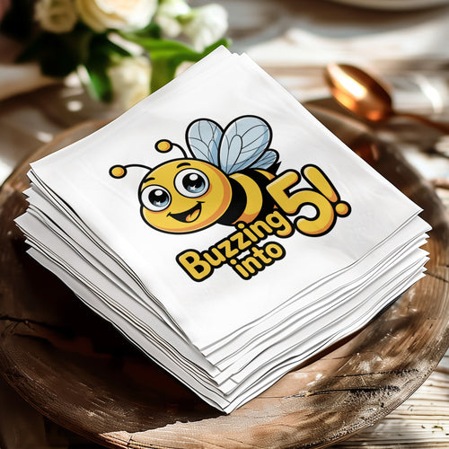 White paper napkins stacked on a wooden plate, featuring a cartoon bee and "Buzzing into 5!".