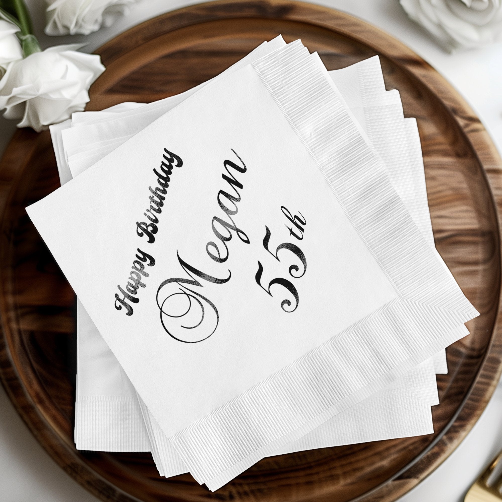 White napkins with "Happy Birthday Megan 55th" in black lettering.