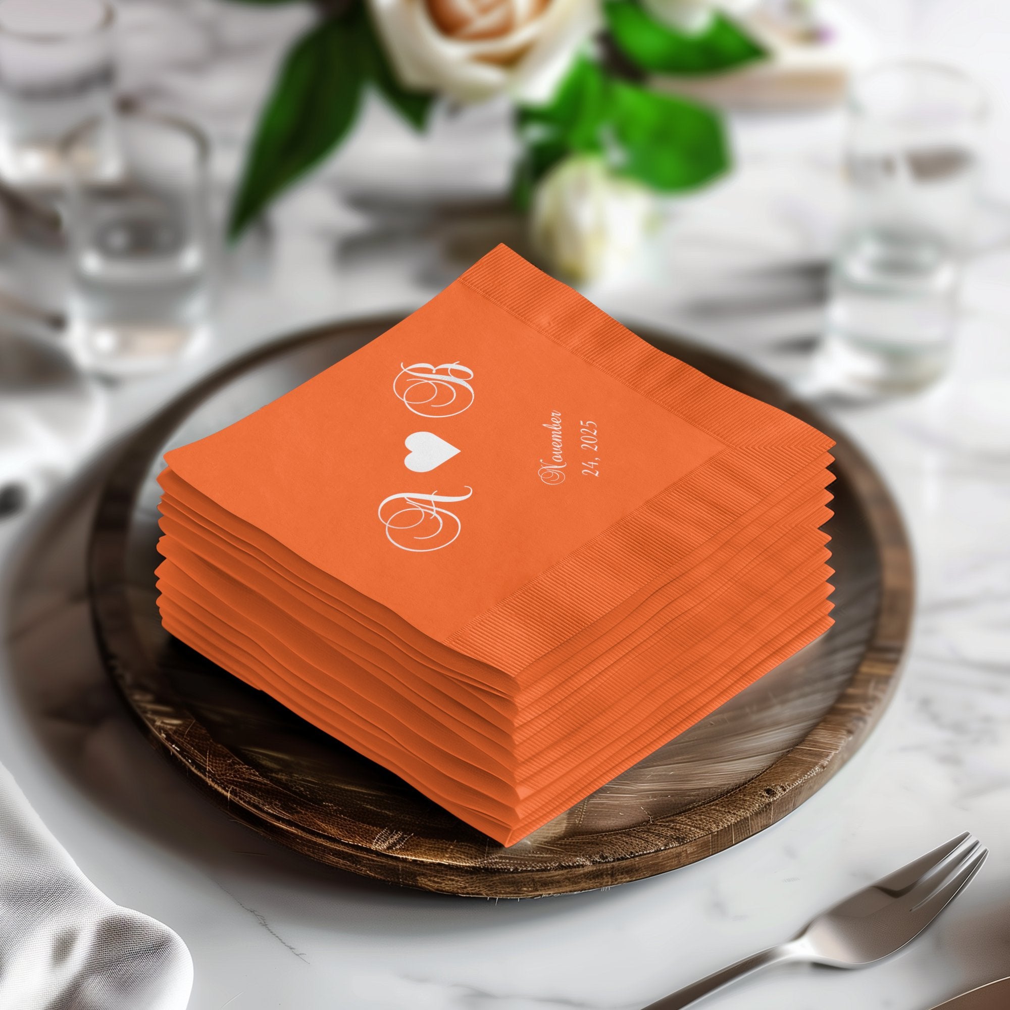 Orange wedding napkins stacked on a wooden charger with initials and date.