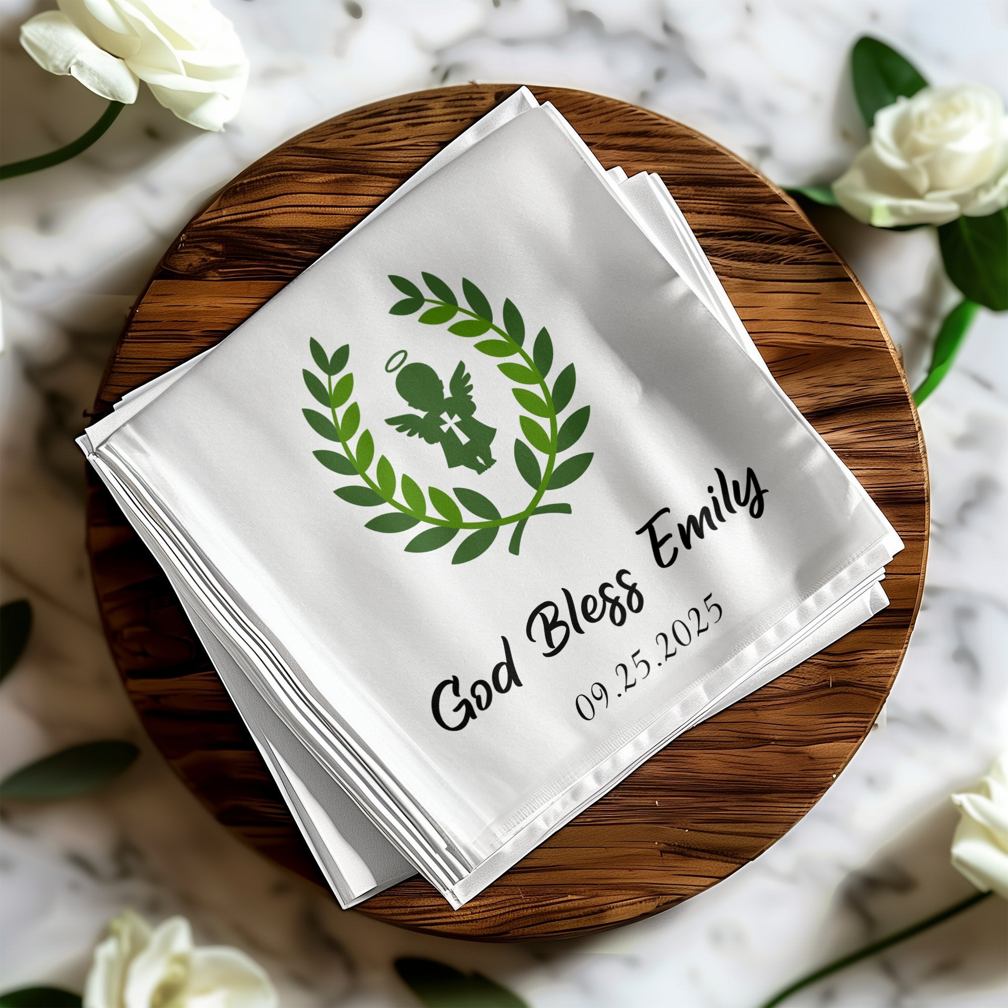 White linen napkin with "God Bless Emily" and a date, framed by a green laurel wreath.